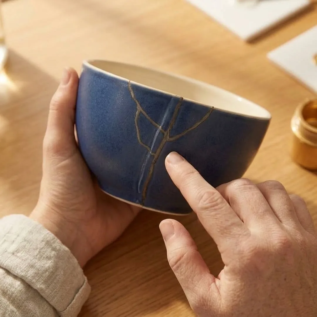 Hands holding a glued indigo bowl, one finger following the seam that will carry the gold